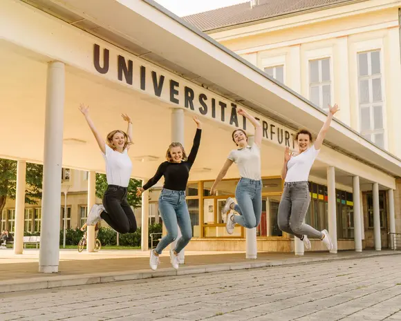 Springende Studentinnen vorm Eingangsbereich der Uni Erfurt