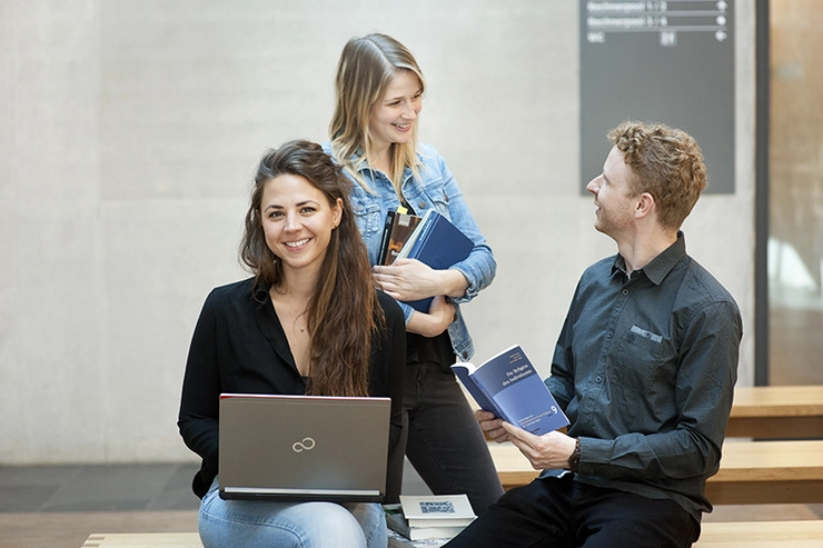 Drei Personen mit Büchern und Laptop