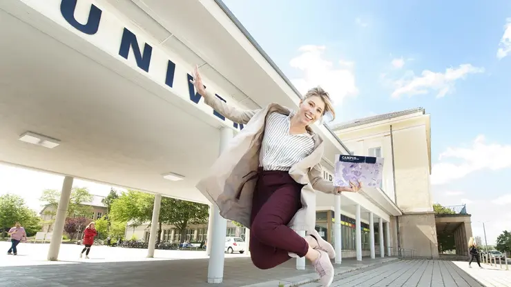 Eine Studierende hüpft vorm Haupteingang der Uni