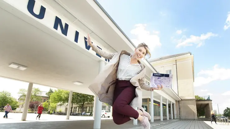 Eine Studierende hüpft vorm Haupteingang der Uni