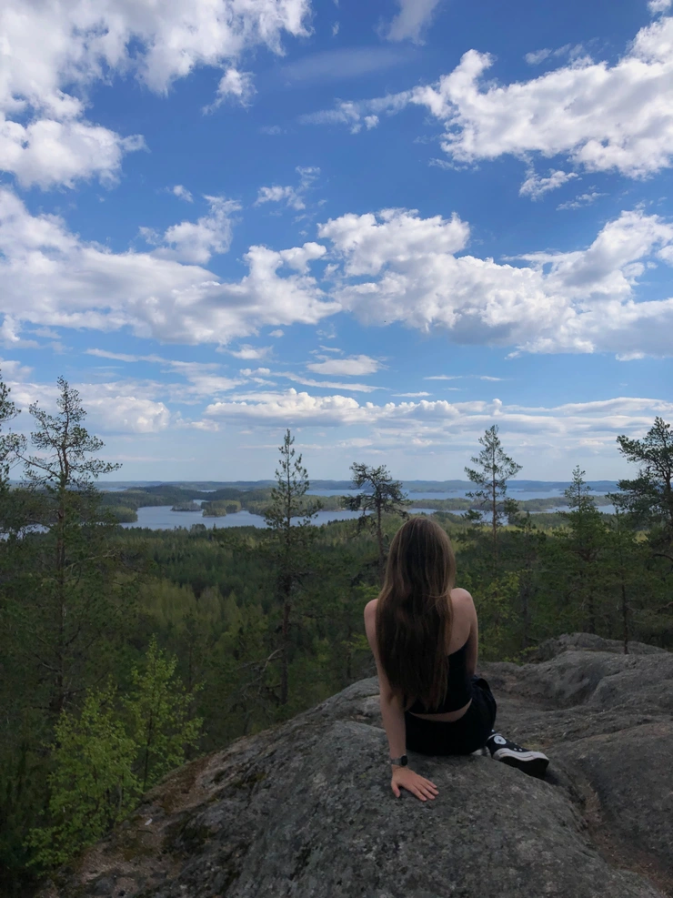 Person sitzt auf einem Aussichtspunkt, Wald und Himmel