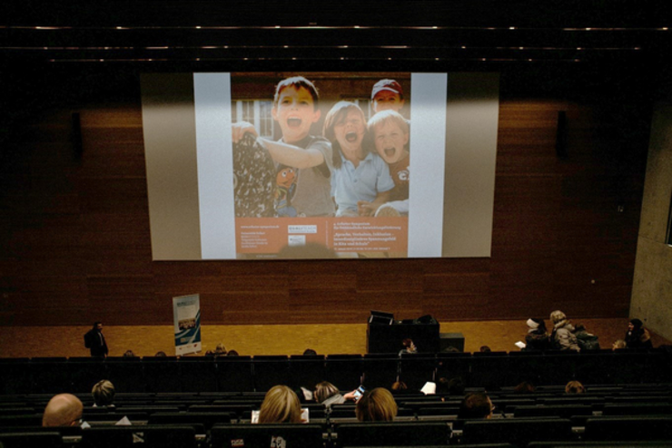 Motto "Verhalten, Sprache, Inklusion – interdisziplinäres Spannungsfeld in Kita und Schule" des 4. Erfurter Symposium wird an eine Leinwand im Hörsaal projiziert