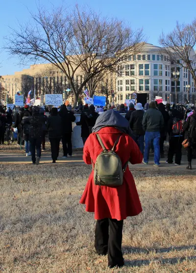 Beyond NoDAPL March on Washington, DC. Woman in red cloth coat as marchers set out from gathering near the Reflecting Pool of the US Capitol