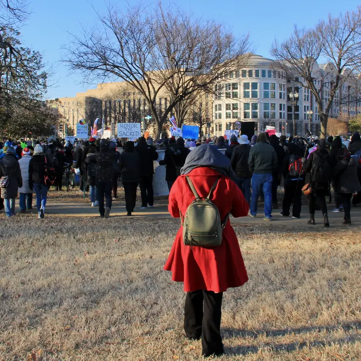 Beyond NoDAPL March on Washington, DC. Woman in red cloth coat as marchers set out from gathering near the Reflecting Pool of the US Capitol.