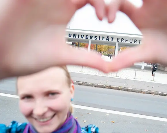 Frau formt mit den Händen ein Herz vor der Universität Erfurt